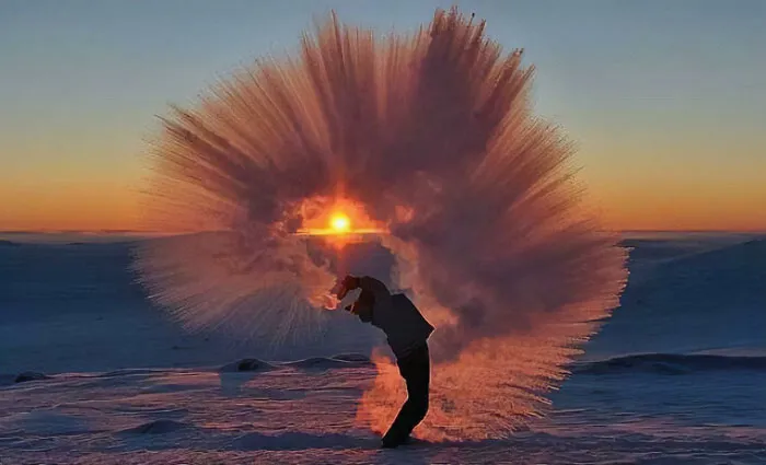 Persona lanzando agua congelada al aire al atardecer creando efecto de surrealismo en paisaje nevado.