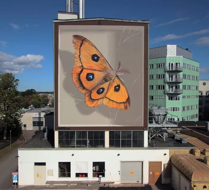 A hyper-realistic mural of an accurate butterfly painted by a French artist on a large building wall.