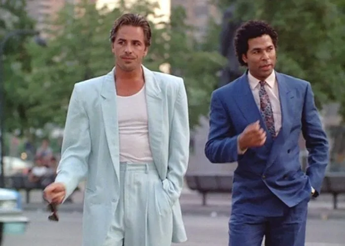 Men wearing pastel and dark suits, showcasing 80s fashion trends with loose fits and bold colors in an urban setting.