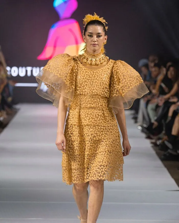 A model walks the runway in a dress designed by an 8-year-old fashion prodigy, showcasing a creative and intricate garment.