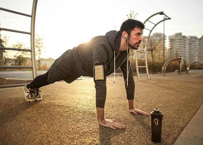 Man doing push-ups outdoors, listening to music, illustrating life cheat codes for effective workouts.