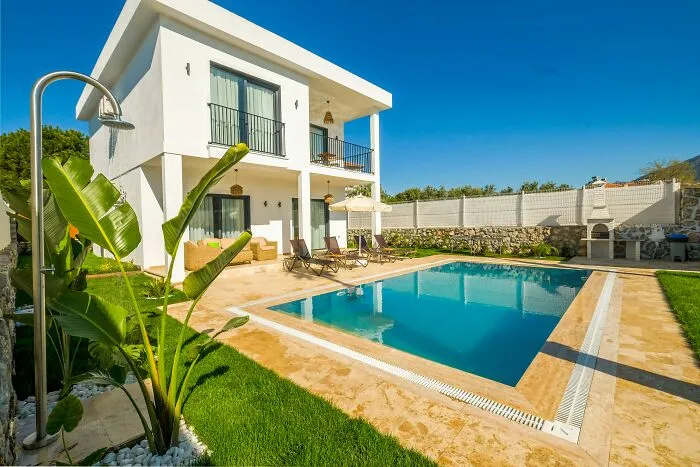 Modern house with a pool and patio, surrounded by greenery, under a clear blue sky.