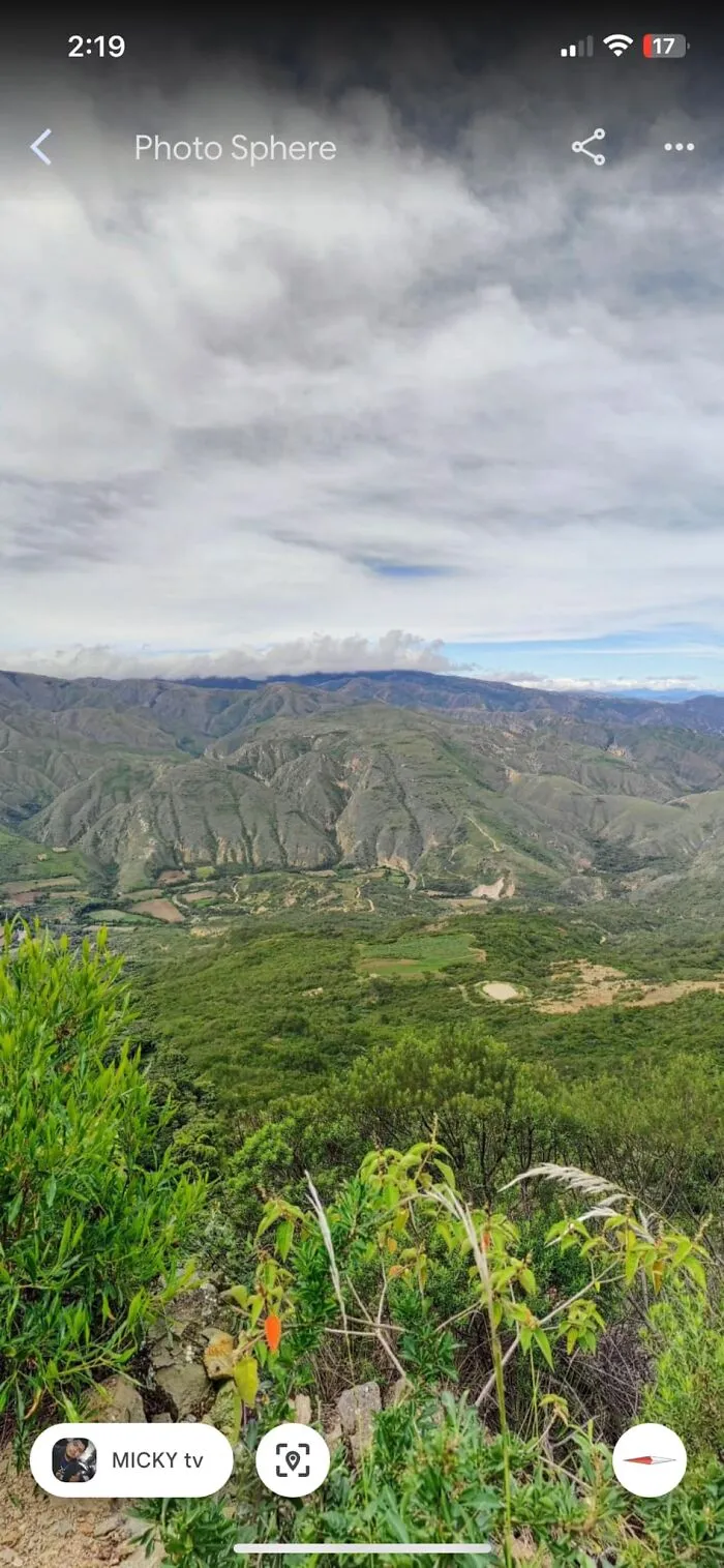 Strange mountain formations captured on Google Earth with greenery in the foreground under a cloudy sky.