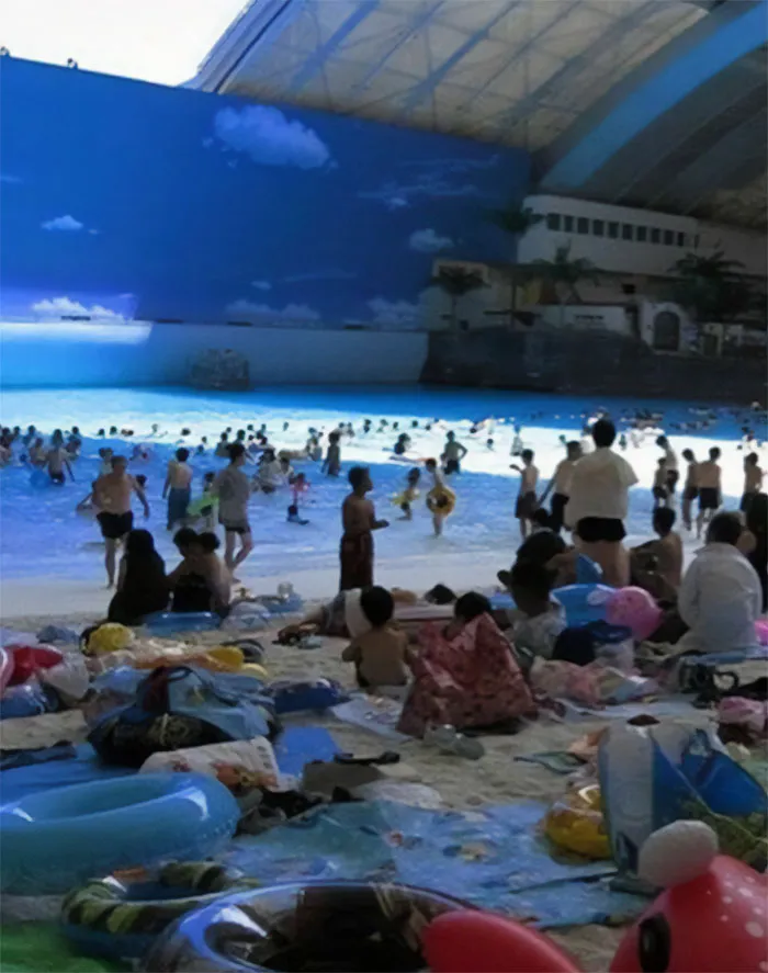 Indoor beach scene with people enjoying artificial waves, symbolizing humans of capitalism in leisure spaces.
