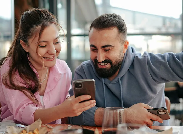 A woman and man smiling at a phone, reminiscent of high school reminiscing, in a casual setting.