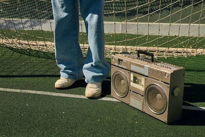 Teen standing on a sports field with a retro boombox, highlighting generational disconnect.