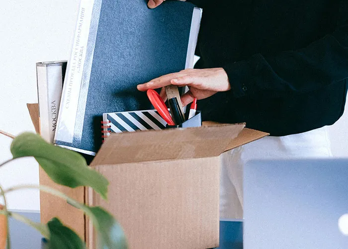 Person packing office supplies into a cardboard box, symbolizing a work-related change or revenge against a boss.