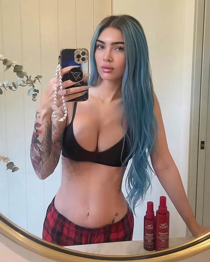 Person with long blue hair in a black top taking a mirror selfie, showcasing a natural look.