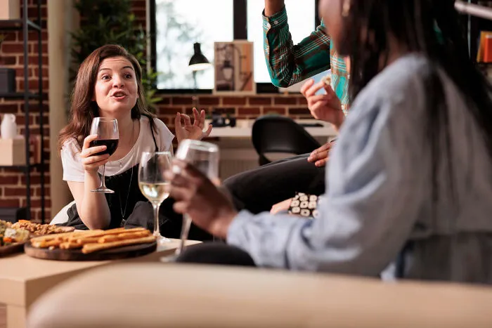 People enjoying wine and snacks in a cozy living room setting, engaging in animated conversation.