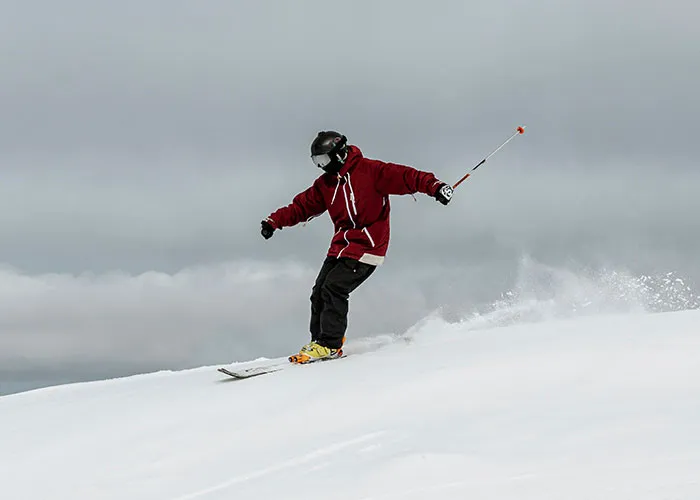 Person skiing down a snowy slope, wearing a red jacket and helmet, representing adventurous hikes.