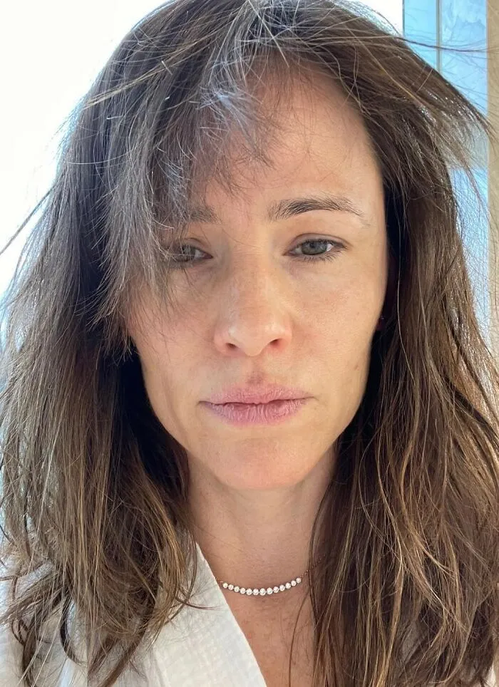 Celebrity with no makeup, natural hair, wearing a pearl necklace in a bright setting.