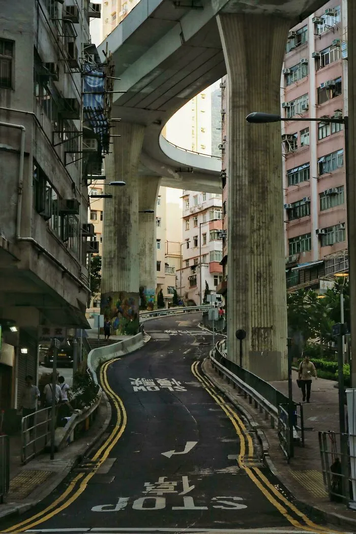 Calle urbana estrecha bajo un puente elevado, representando el infierno urbano moderno.