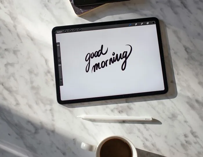 Tablet displaying "good morning" on marble surface beside a cup of coffee. Social rules people ignore in morning routines.
