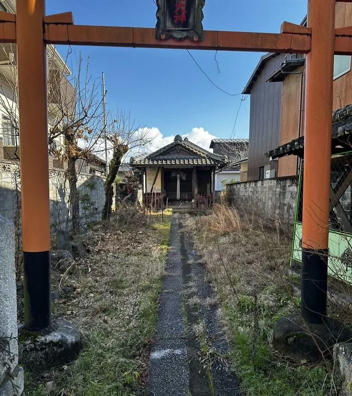 Traditional Japanese shrine behind an orange torii gate under a clear blue sky, showcasing unique cultural architecture.