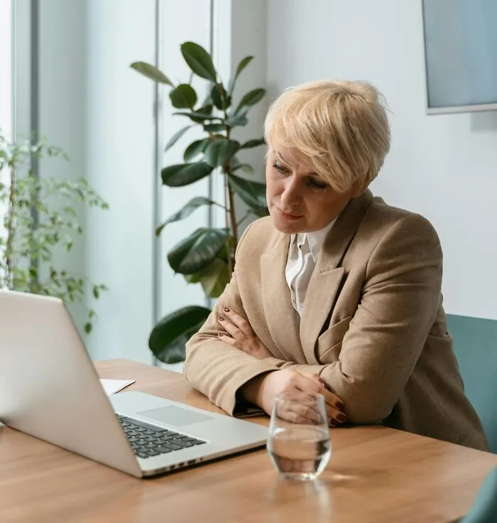 Person in a beige blazer looking at a laptop in an office setting.
