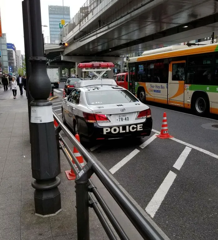 Police car parked on a busy Japan street, with traffic cones and buses nearby.