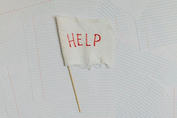 A white flag with "HELP" written on it sticks out from a stack of lined paper, humorously depicting office distress.