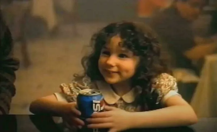 A smiling child in a floral dress enjoys a soda, capturing a joyful '90s moment.