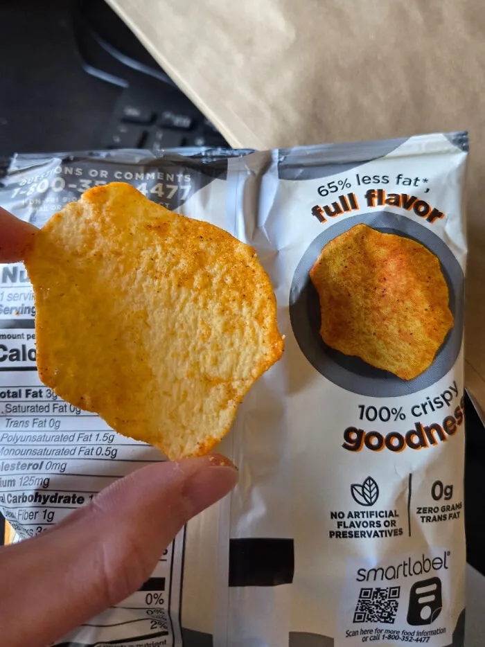 Hand holding a potato chip that perfectly matches the image on the chip bag showing something moderately interesting.