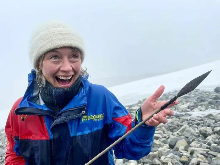 Person smiling and holding an ancient artefact in snowy landscape, wearing a colorful jacket and wool hat.
