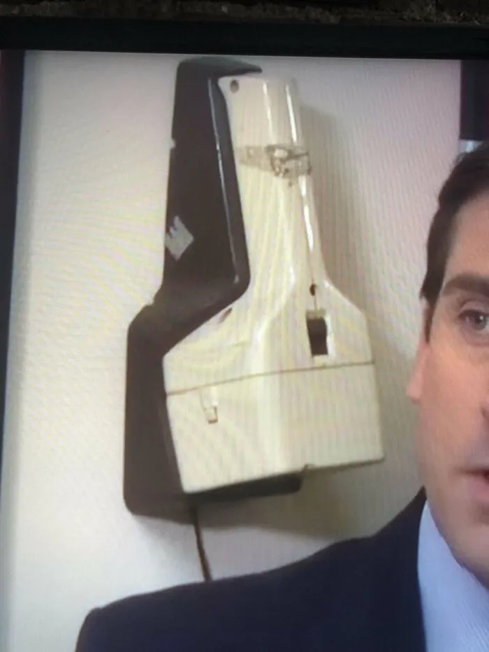 What’s This Thing In The Background Of The Office? Light Beige Plastic, Has A Brown Wall Mount And What Looks Like A Cord. Was In The Kitchen Area