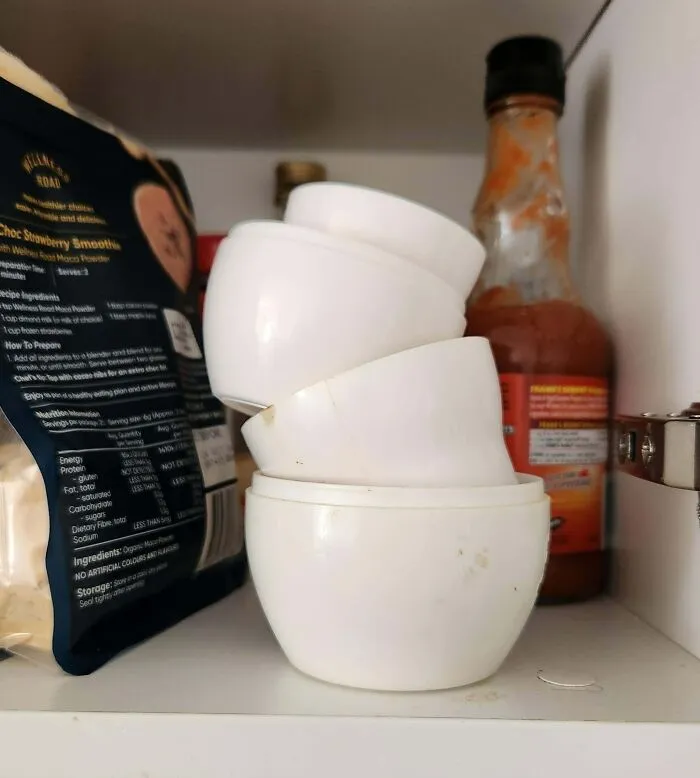 Tazones de plástico apilados desordenadamente en un estante con salsa picante al fondo.