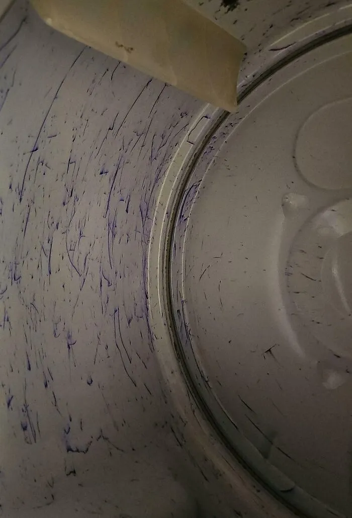 Interior de una lavadora con manchas azules, ilustrando ejemplos de maridos comportándose de manera descuidada.