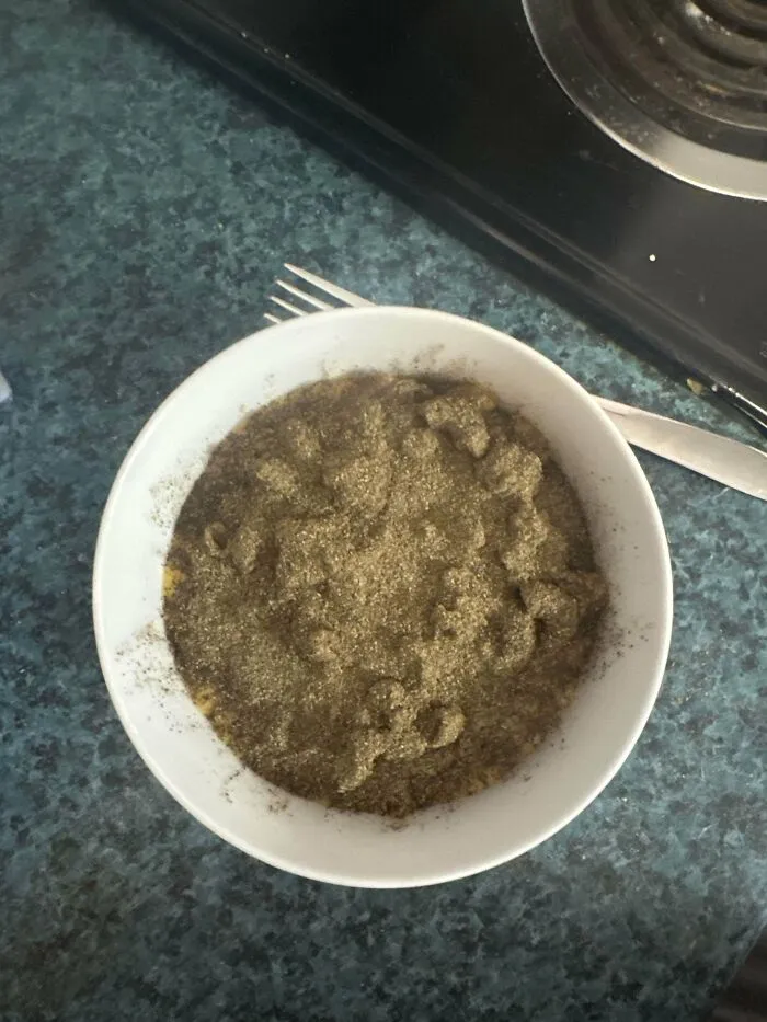 Bowl of macaroni noodles covered in excessive black pepper sitting on a kitchen counter showing a stupid dish.