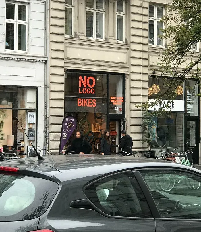 Tienda de alquiler de bicicletas sin logo en ciudad europea con viajeros sorprendidos por lo diferente en otros países.