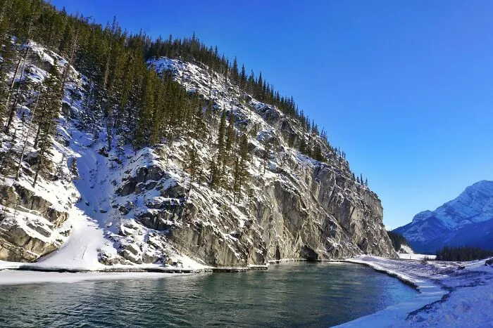 Paisaje de Canadá con río, nieve y montañas al fondo bajo un cielo despejado.