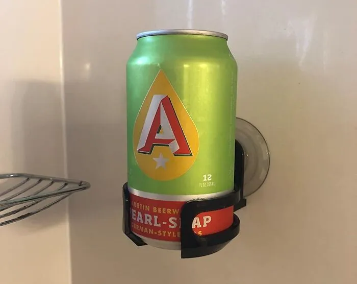 A beer can creatively held by a wall-mounted suction cup in a shower, adding goofiness to the day.