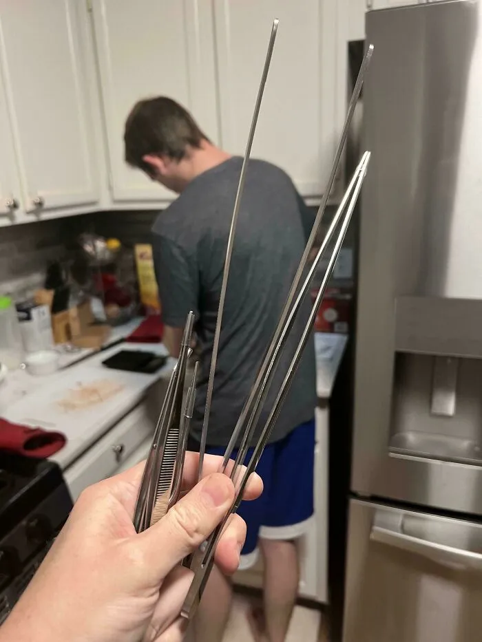 Hand holding kitchen tools in a food service setting, with a person preparing in the background.