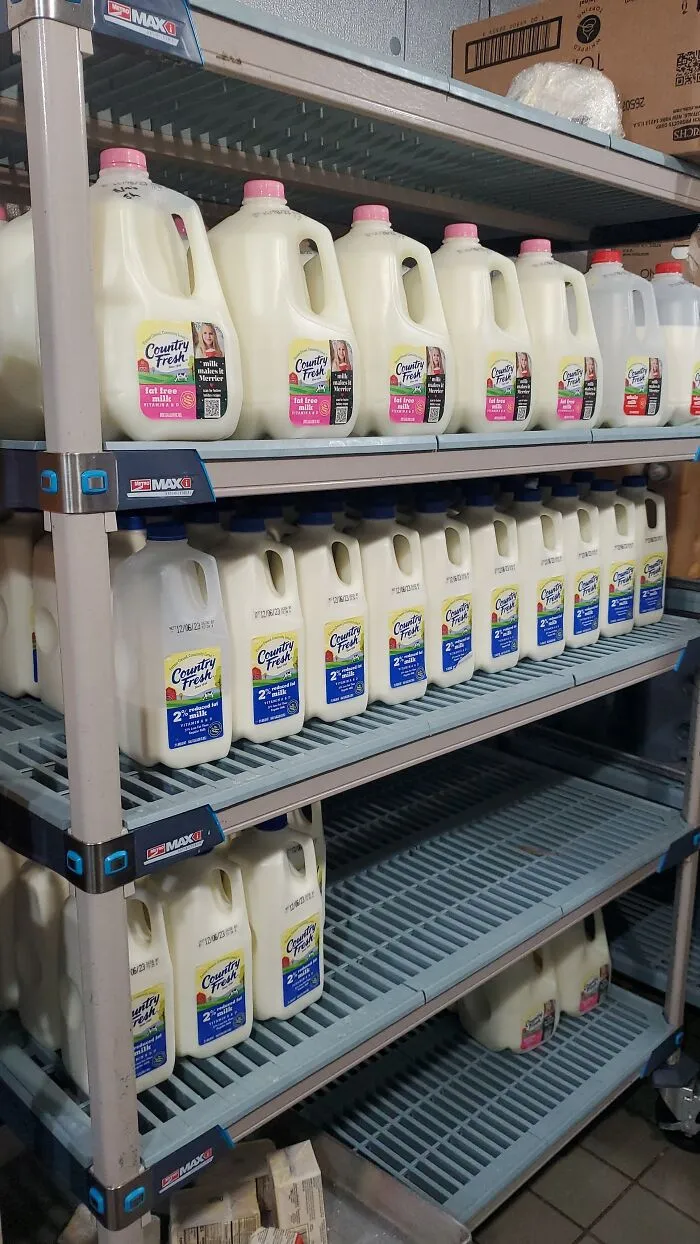 Milk cartons stacked on metal shelves in a food service industry setting.