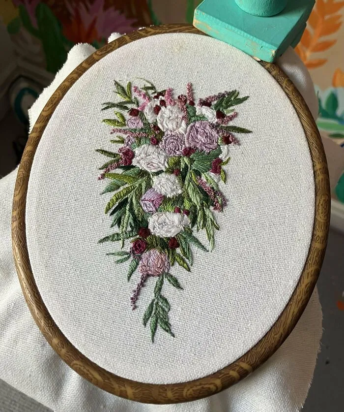 Intricate and beautiful embroidery of flowers and leaves displayed in a wooden hoop by skilled hands.
