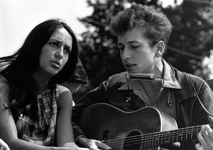 Two people singing outdoors, one playing guitar and harmonica, representing famous singers.