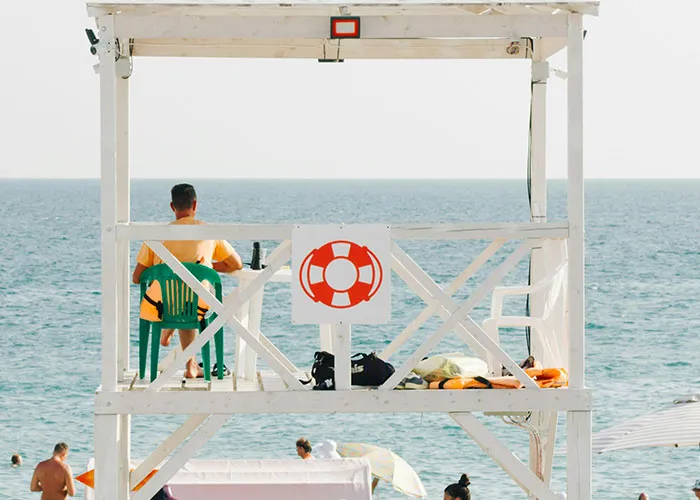 Lifeguard in a tower by the sea, wearing a yellow shirt, symbolizing calm and vigilance against bosses.