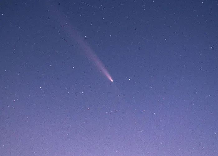 A comet streaks across a starry night sky, its tail glowing brightly.