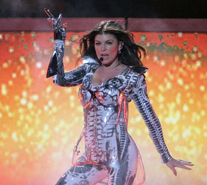 Singer performing energetically on stage in a futuristic silver outfit.