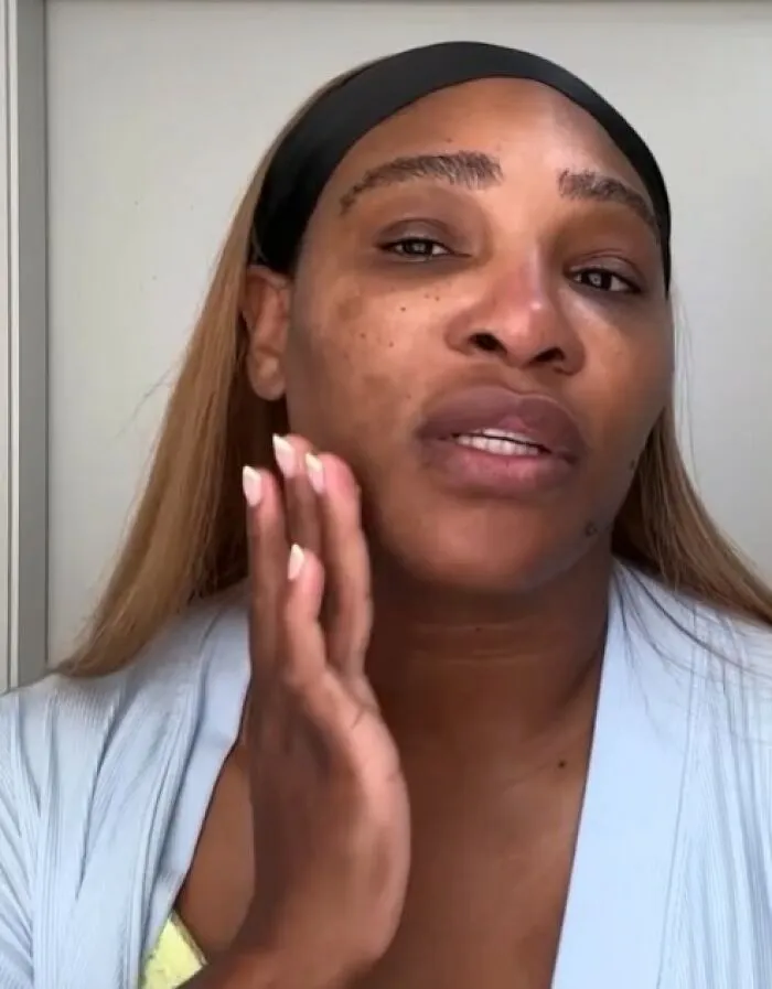 Celebrity without makeup, wearing a headband and robe, touching face.