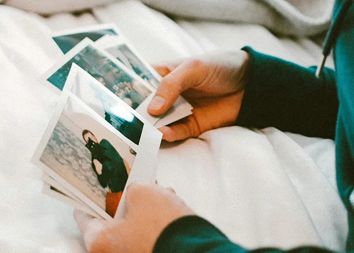 Hands holding and flipping through a stack of Polaroid photos on a bed, illustrating personal memories.