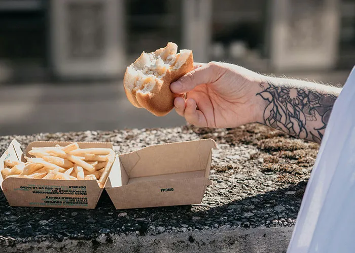 Tattooed arm holding a burger with fries, emphasizing considerations before getting inked.