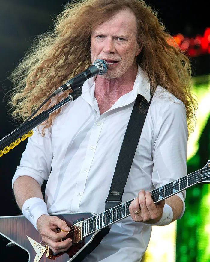 Musician performing on stage with a guitar, wearing a white shirt, controversial opinions on singers' success.