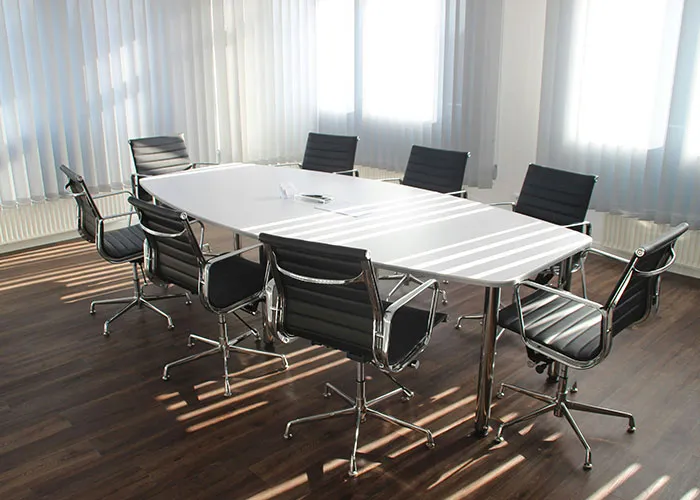 Empty conference room with a long table and chairs, sunlight streaming through blinds, symbolizing workplace dynamics.