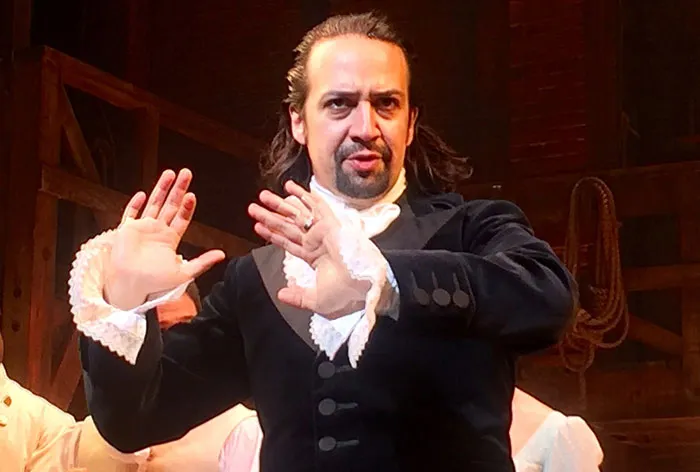 A performer in historical attire on stage, gesturing expressively.