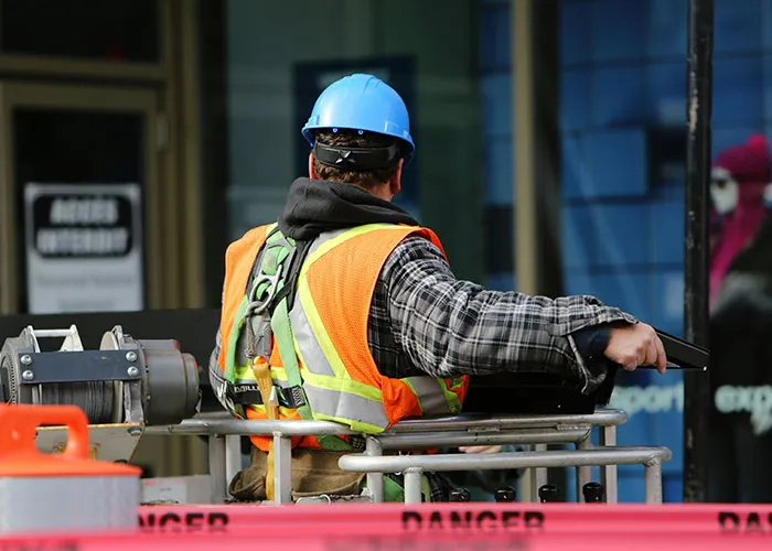Construction worker in safety gear on lift near a "Danger" sign, highlighting workplace safety and caution.