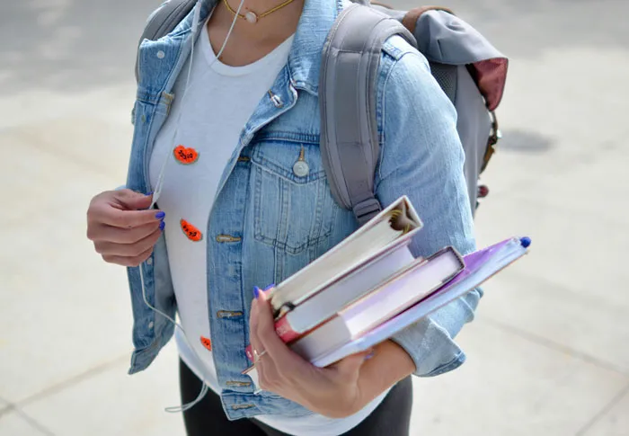 Person carrying books and wearing a denim jacket, suggests rich people might overlook common lifestyle needs.
