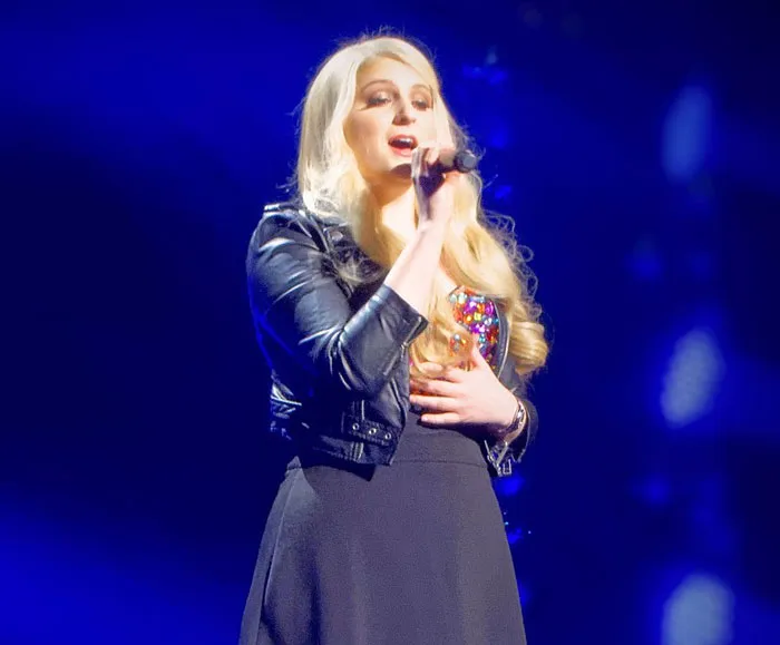 Blonde singer on stage in a black dress and jacket, holding a microphone under bright lights, main SEO keyword discussed.