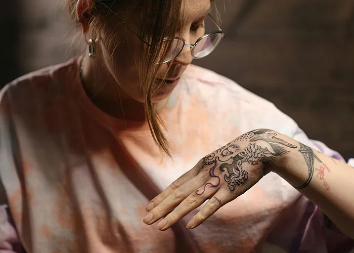 Person with glasses examining a detailed tattoo on their hand, a step before getting inked.