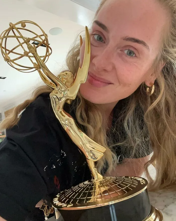 Celebrity smiling without makeup, holding a golden award in a casual setting.