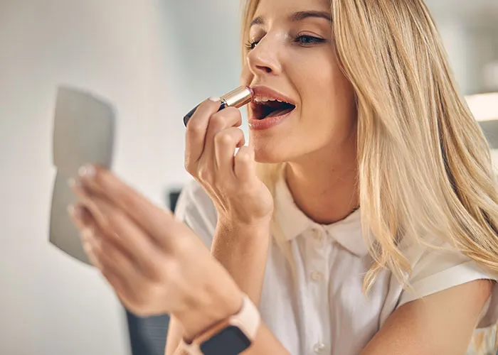 Woman applying lipstick, learning beauty tips, wearing a white shirt, highlighting a common revelation for partners.